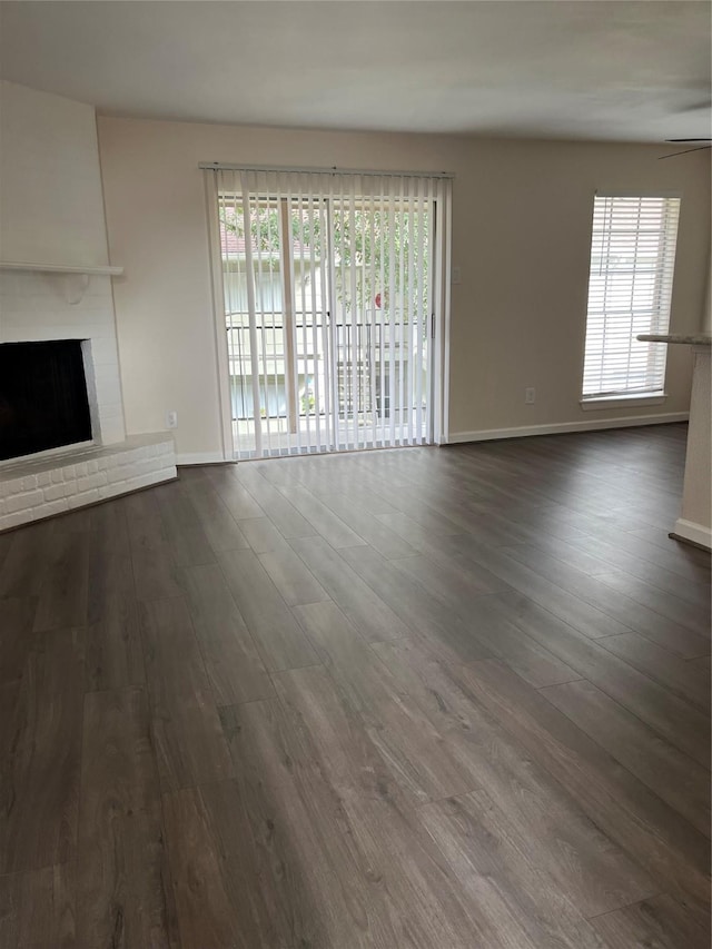 unfurnished living room featuring ceiling fan, a fireplace, and dark wood-type flooring