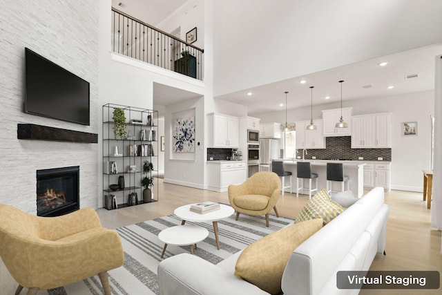 living room featuring a stone fireplace, a high ceiling, and light wood-type flooring