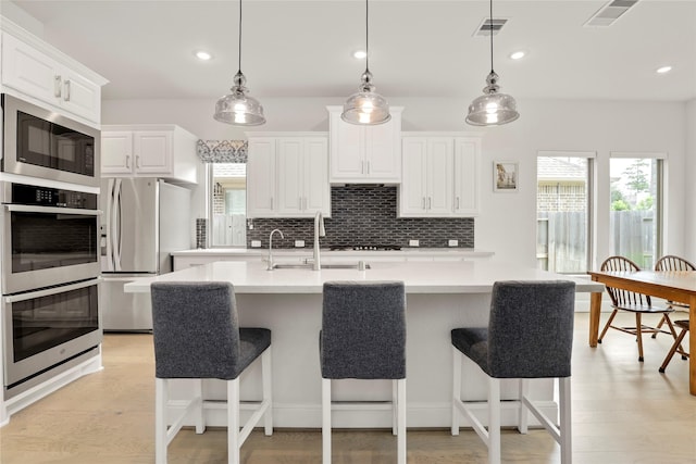 kitchen with light hardwood / wood-style floors, an island with sink, pendant lighting, and appliances with stainless steel finishes