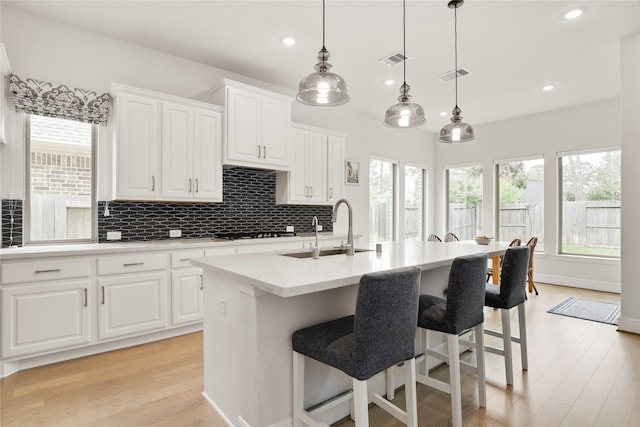 kitchen featuring sink, decorative light fixtures, a center island with sink, white cabinets, and light hardwood / wood-style floors