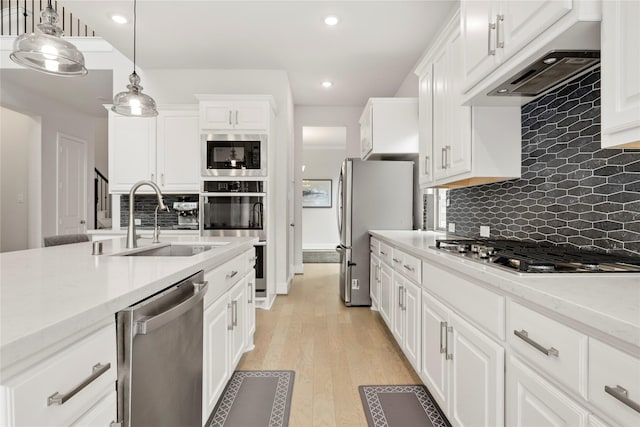 kitchen featuring appliances with stainless steel finishes, light wood-type flooring, sink, decorative light fixtures, and white cabinetry