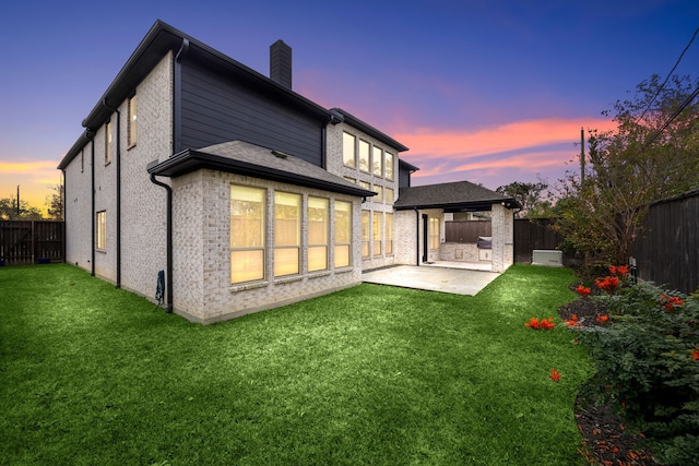 back house at dusk featuring a yard and a patio area