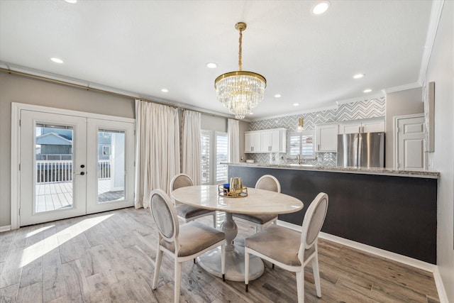 dining area with a chandelier, light wood-type flooring, crown molding, and french doors