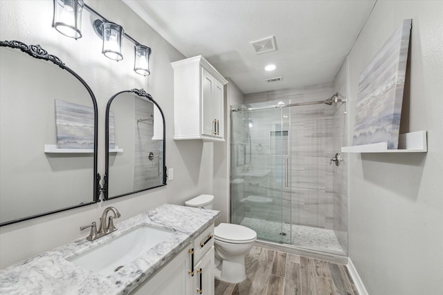 bathroom featuring a shower with door, vanity, wood-type flooring, and toilet