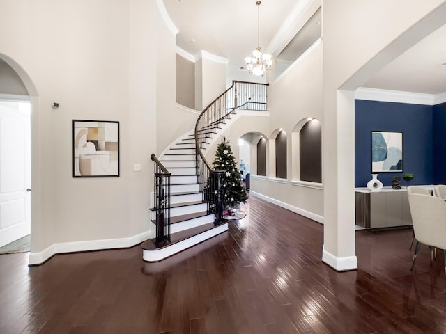 entrance foyer with a notable chandelier, ornamental molding, dark wood-type flooring, and a high ceiling