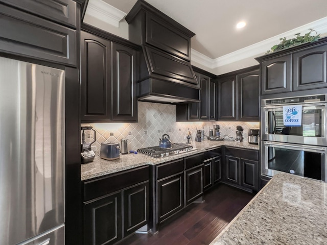 kitchen featuring dark wood-type flooring, crown molding, decorative backsplash, light stone countertops, and appliances with stainless steel finishes