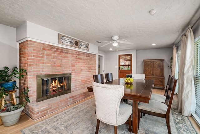 dining space with a brick fireplace, hardwood / wood-style flooring, a textured ceiling, and ceiling fan