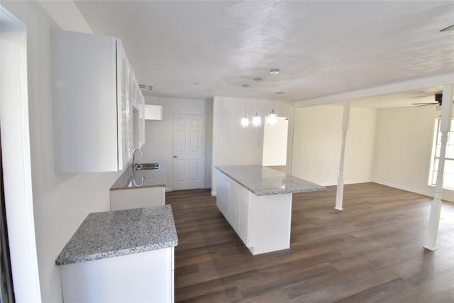 kitchen featuring a center island, light stone counters, dark hardwood / wood-style floors, decorative light fixtures, and white cabinets