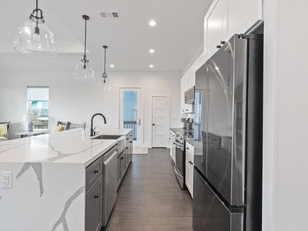 kitchen with stainless steel appliances, sink, white cabinets, decorative light fixtures, and light stone counters