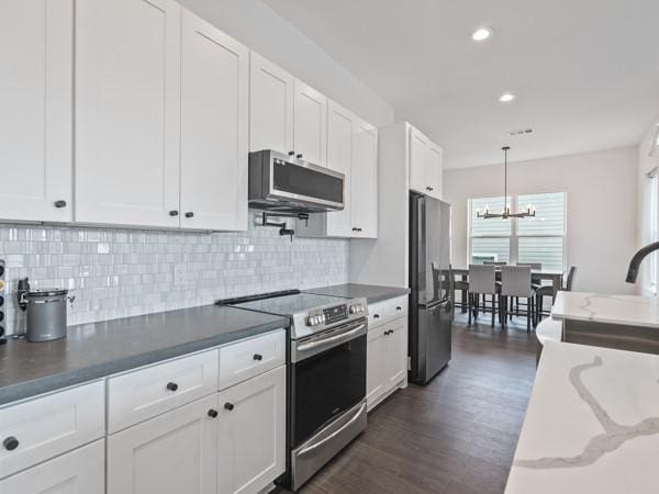 kitchen with white cabinets, decorative backsplash, dark hardwood / wood-style floors, pendant lighting, and appliances with stainless steel finishes