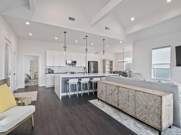 kitchen featuring stainless steel refrigerator, hanging light fixtures, a large island with sink, decorative backsplash, and white cabinets