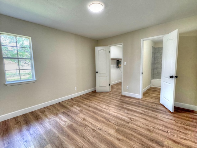 unfurnished bedroom with light hardwood / wood-style floors, a spacious closet, and connected bathroom