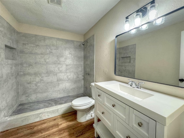 bathroom with a tile shower, vanity, a textured ceiling, hardwood / wood-style flooring, and toilet