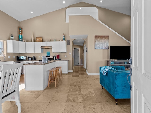 kitchen with a breakfast bar, stainless steel appliances, high vaulted ceiling, a center island, and white cabinetry