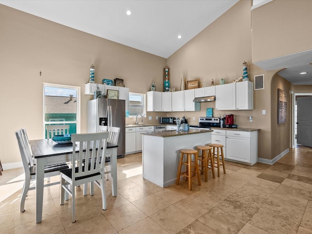 kitchen featuring appliances with stainless steel finishes, a breakfast bar, a kitchen island, high vaulted ceiling, and white cabinetry