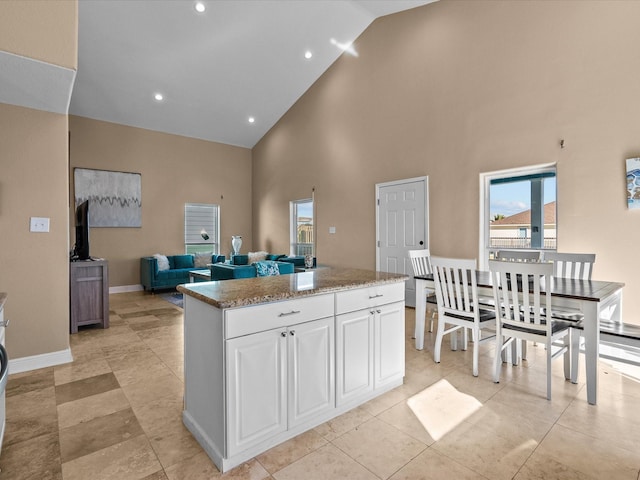 kitchen with light stone countertops, a center island, white cabinets, and high vaulted ceiling