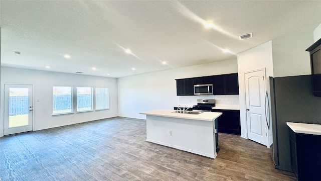 kitchen with appliances with stainless steel finishes, a textured ceiling, a kitchen island with sink, dark wood-type flooring, and sink