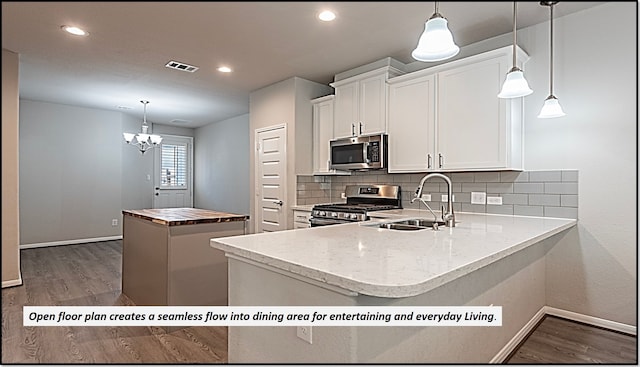 kitchen featuring kitchen peninsula, stainless steel appliances, sink, decorative light fixtures, and white cabinets