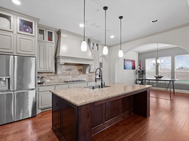 kitchen featuring sink, premium range hood, stainless steel appliances, light stone counters, and decorative light fixtures