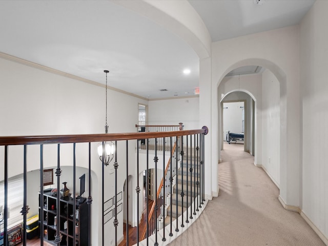 hallway featuring a notable chandelier, crown molding, and light colored carpet