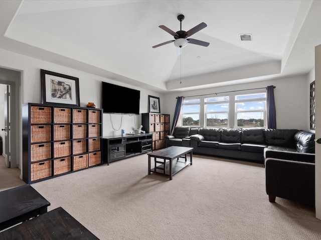 living room with a tray ceiling, ceiling fan, and carpet