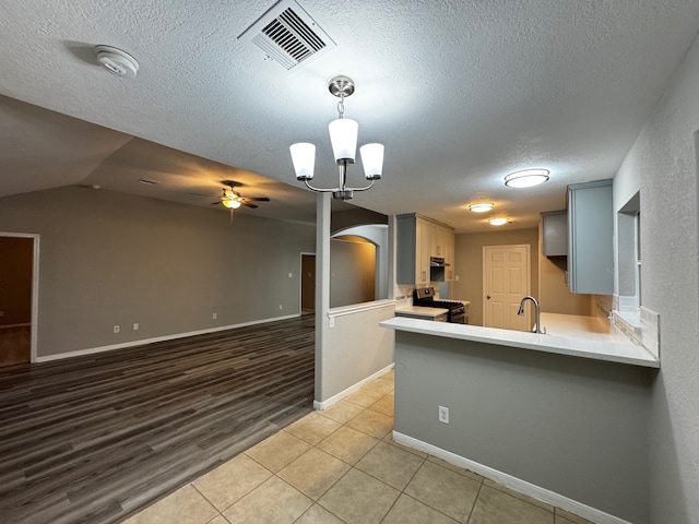 kitchen with kitchen peninsula, a textured ceiling, ceiling fan with notable chandelier, vaulted ceiling, and light hardwood / wood-style floors