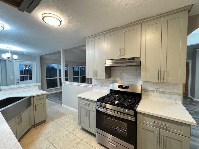 kitchen featuring gray cabinetry, sink, stainless steel range with gas cooktop, decorative backsplash, and light tile patterned floors