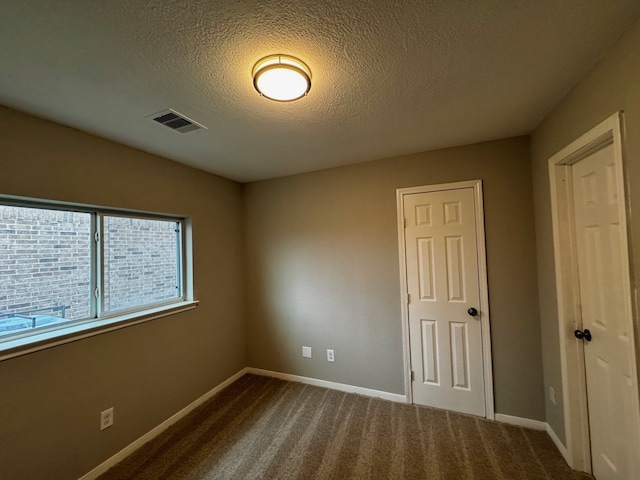 unfurnished room with a textured ceiling and dark carpet