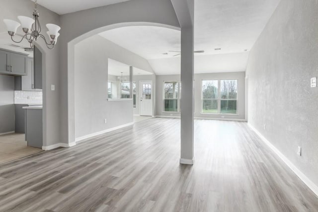 unfurnished living room with ceiling fan with notable chandelier and light hardwood / wood-style flooring