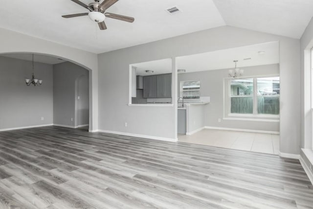 unfurnished living room with vaulted ceiling, ceiling fan with notable chandelier, and hardwood / wood-style floors