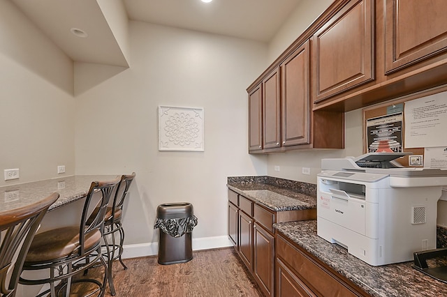 kitchen with light hardwood / wood-style flooring, a breakfast bar area, and dark stone countertops