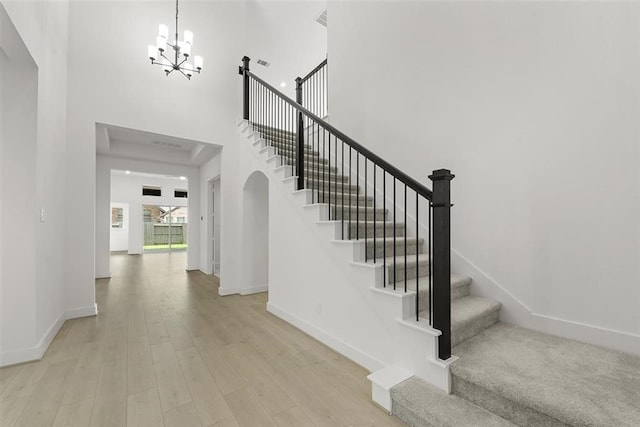 staircase featuring hardwood / wood-style floors, a towering ceiling, and an inviting chandelier