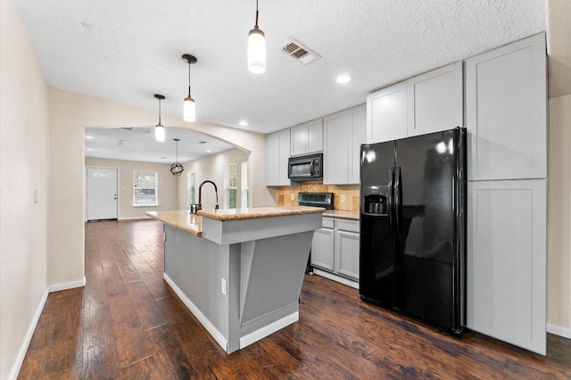 kitchen with decorative light fixtures, an island with sink, tasteful backsplash, and black appliances