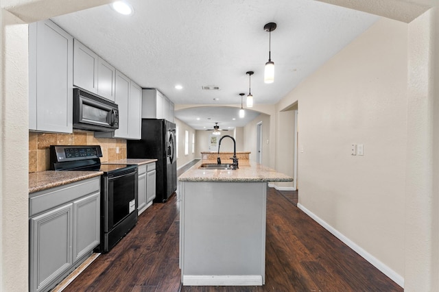 kitchen with sink, tasteful backsplash, pendant lighting, a kitchen island with sink, and black appliances