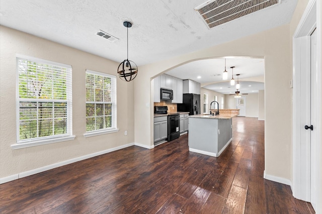 kitchen featuring an island with sink, light stone counters, hanging light fixtures, and black appliances