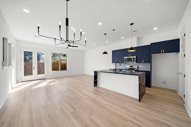 kitchen featuring blue cabinets, light wood-type flooring, an island with sink, tasteful backsplash, and stainless steel appliances