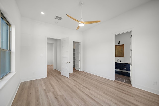 unfurnished bedroom with ensuite bath, ceiling fan, sink, a walk in closet, and light wood-type flooring