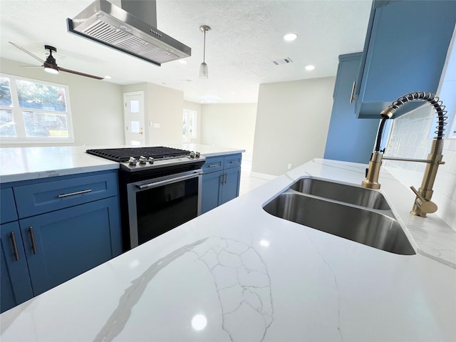 kitchen with wall chimney range hood, sink, blue cabinetry, decorative light fixtures, and stainless steel range with gas stovetop