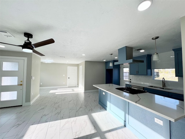 kitchen with gas cooktop, a textured ceiling, blue cabinets, sink, and hanging light fixtures