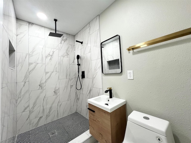 bathroom with tiled shower, vanity, and toilet