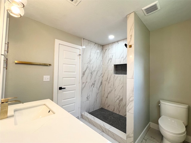 bathroom featuring a tile shower, sink, a textured ceiling, and toilet