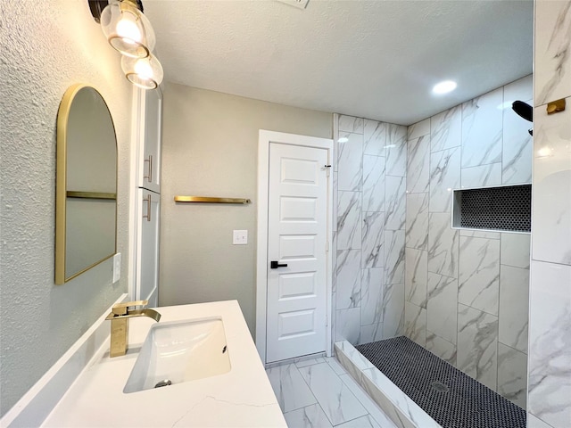 bathroom featuring a textured ceiling, vanity, and tiled shower