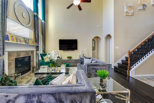 living room featuring a tiled fireplace, plenty of natural light, a towering ceiling, and hardwood / wood-style floors