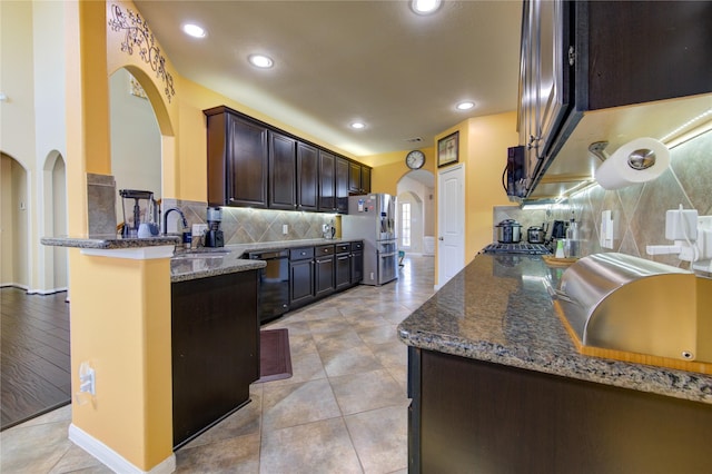 kitchen featuring kitchen peninsula, dark stone counters, dark brown cabinetry, sink, and black appliances