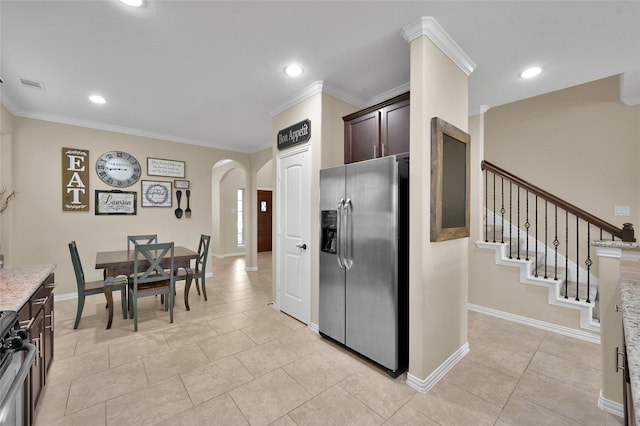 kitchen featuring light tile patterned floors, appliances with stainless steel finishes, dark brown cabinets, light stone counters, and ornamental molding