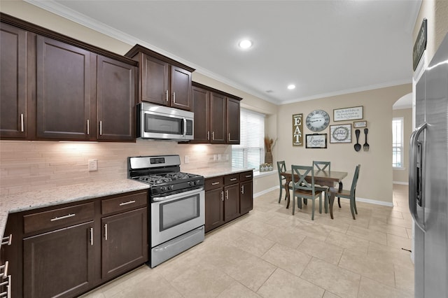 kitchen with tasteful backsplash, dark brown cabinets, ornamental molding, stainless steel appliances, and light stone countertops