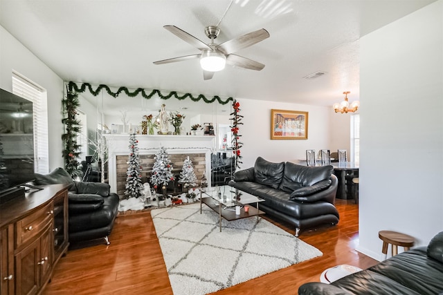 living room featuring hardwood / wood-style flooring, ceiling fan with notable chandelier, and a brick fireplace