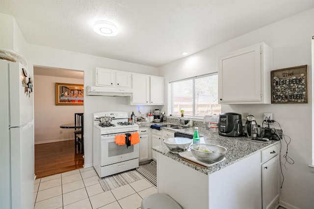 kitchen with white appliances, sink, light tile patterned floors, light stone counters, and white cabinetry