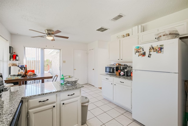 kitchen with a textured ceiling, white refrigerator, white cabinetry, and light stone counters