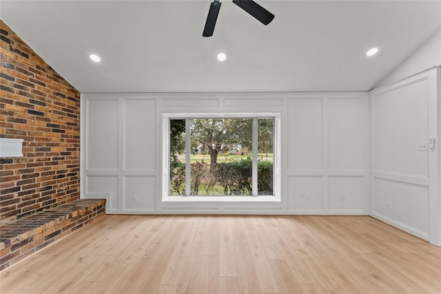 unfurnished living room with light hardwood / wood-style floors, vaulted ceiling, ceiling fan, and brick wall